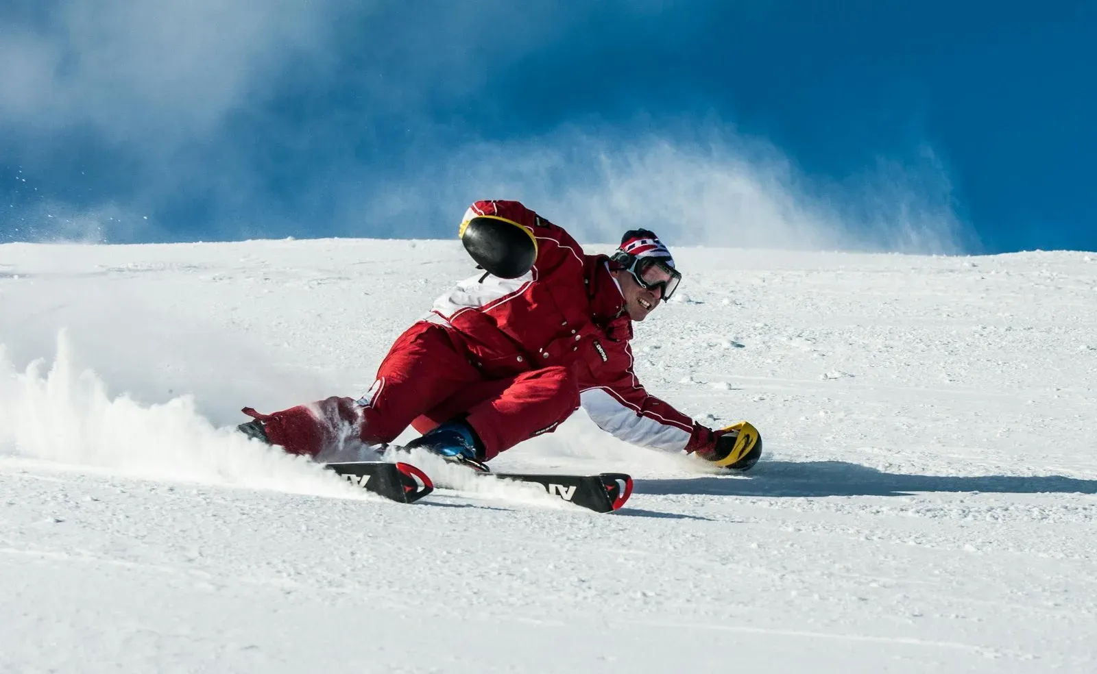 A skier in vibrant red gear skillfully navigates a snowy slope on a sunny day.
