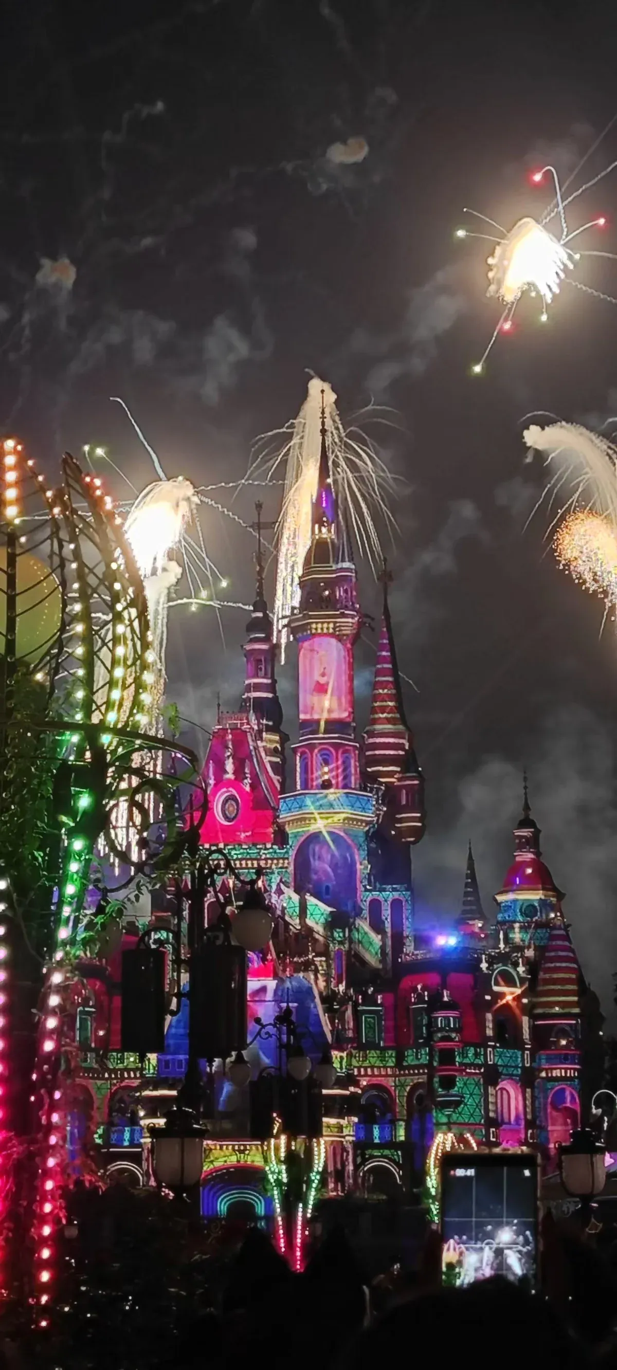 The Enchanted Storybook Castle lit in pink, green and blue at night with fireworks bursting above it
