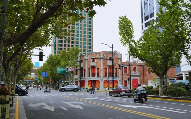 Plane trees over a wide Shanghai street, with a red-brick 1920s building and new towers behind the traffic