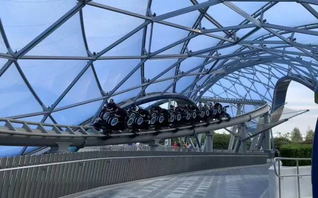A train of riders on TRON Lightcycle Power Run speeding along a curved track under the park's blue glass canopy