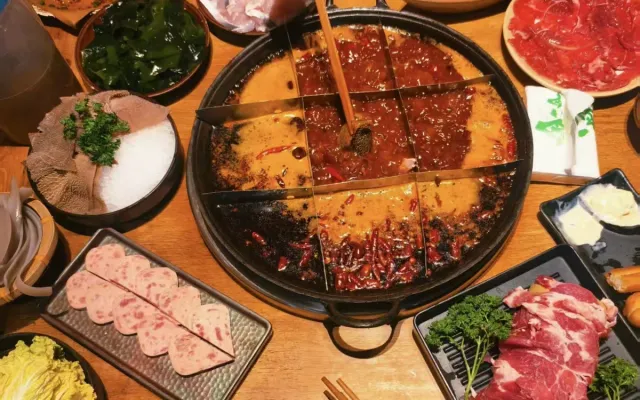A nine-grid hotpot pot on a wooden table, ringed with plates of tripe, sliced beef, luncheon meat and vegetables