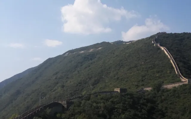 The Great Wall at Mutianyu winding over a densely forested ridge under a clear sky
