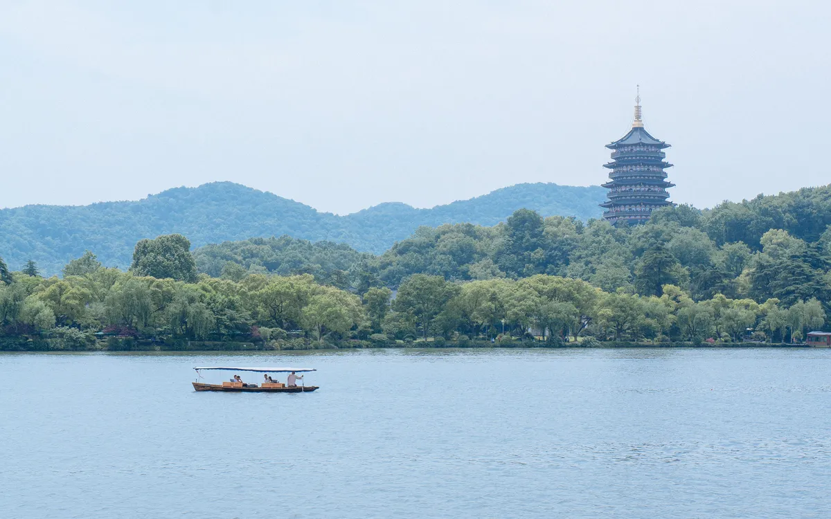 A small boat crossing West Lake in Hangzhou, with Leifeng Pagoda rising above the wooded shore