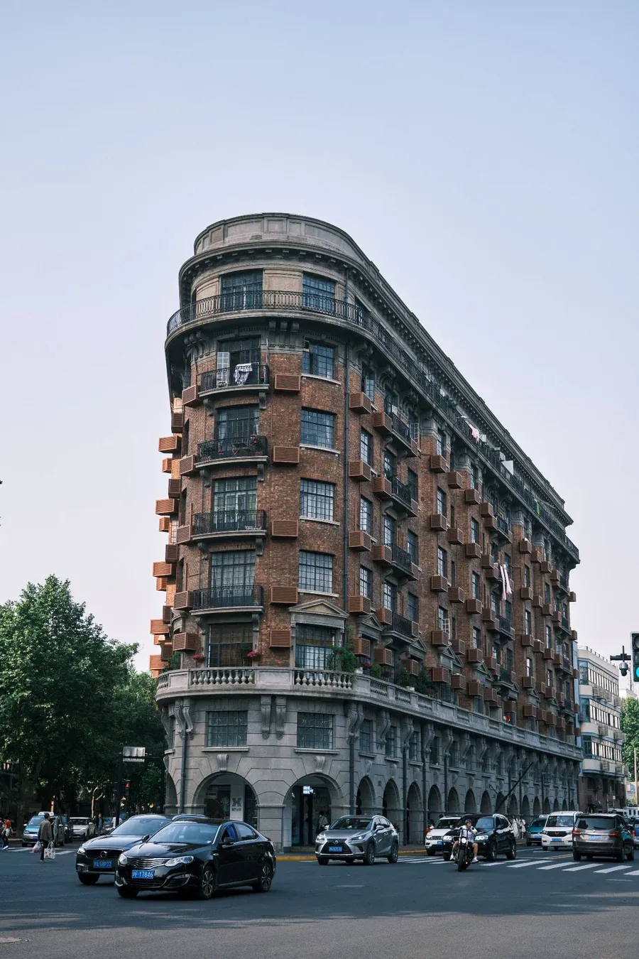 The Wukang Mansion seen from the corner, a curved wedge of red brick and balconies with traffic on the road in front