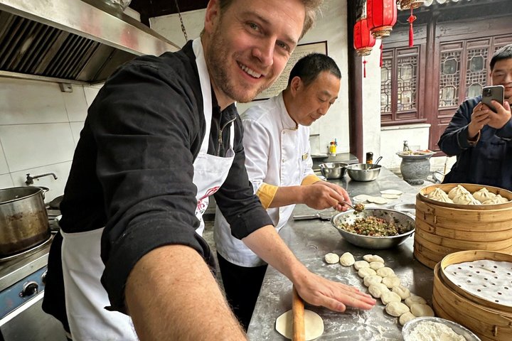 A guest shaping xiaolongbao beside a chef and bamboo steamers