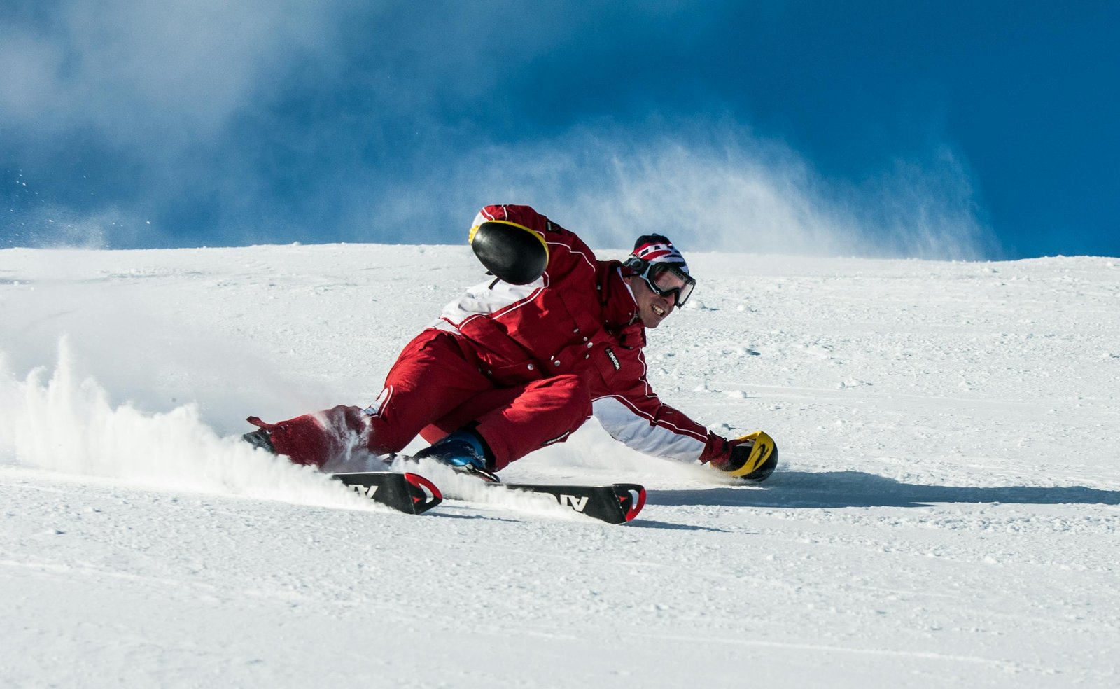 A skier in vibrant red gear skillfully navigates a snowy slope on a sunny day.